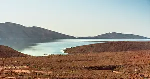 Inlet Prints: Narrow winding inlet of Barrage Al-Hassan Addakhil glistening between rolling red hills in Parc National Al Hassan