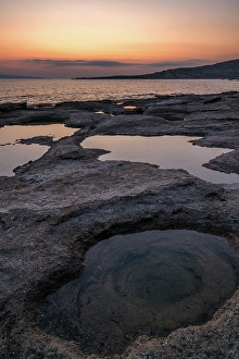 Enchanting Prints: Natural holes in the rocks full of water at sunset, with sea in the background, Greece