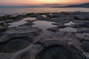 Ripples Prints: Natural holes in the rocks full of water at sunset, with sea in the background, Greece