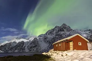 Northern Lights (aurora borealis) illuminate snowy peaks and the wooden cabin