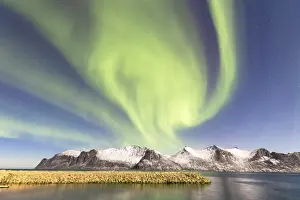 Northern lights (aurora borealis) on snowy peaks and icy sea along Mefjorden seen