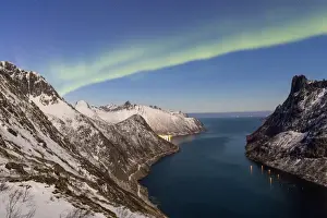 Northern Lights (aurora borealis) on the snowy peaks and the village of Fjordgard