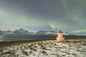 The Northern Lights (aurora borealis) and stars illuminate the lighthouse framed by icy sea