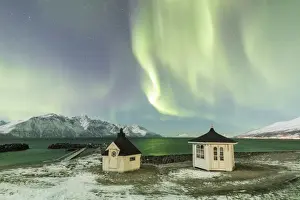 The Northern Lights (aurora borealis) and stars illuminate the wooden huts by icy sea
