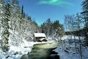 Northern Lights over a chalet overlooking Myllikoski rapids of frozen river, Ruka Kuusamo, Lapland, Finland