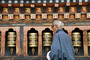Old Bhutanese man turning prayer wheels in Buddhist temple, Thimphu, Bhutan, Asia