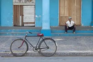 Vinales Prints: Old bicycle propped up outside old building with local man on steps
