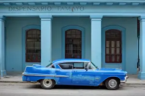 Vintage Car Prints: Old blue American car with body repairs parked in front of blue dispensary