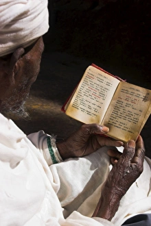 Old man wearing traditional gabi (white shawl) reading Holy Bible in rock-hewn monolithic church of Bet Medhane Alem (Saviour of the World), Lalibela