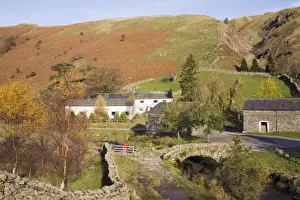 Old stone packhorse bridge over Watendlath Beck with dry stone wall and farm buildings in picturesque village in autumn, Watendlath, Lake District National Park, Cumbria, England, United
