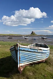 Old wooden fishing boat on a grassy bank with Lindisfarne harbour and Lindisfarne Castle in the background, Holy Island (Lindisfarne), Northumberland, England, United