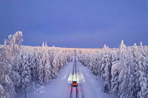 Rural Road Collection: Overhead view of a car driving on empty, icy and slippery road with illuminated headlamps