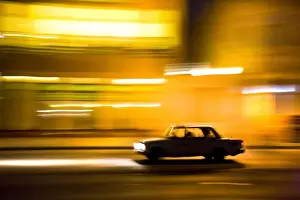 Malecon Prints: Panned shot of car at night passing illuminated buildings on The Malecon