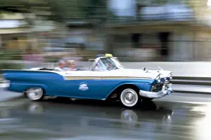 Panned shot of old American car splashing through puddle on Prado, Havana