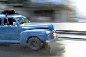 Hispanic Prints: Panned shot of old American car splashing through puddle on Prado, Havana