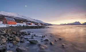 Winter Scene Prints: Panorama of typical wood huts called Rorbu framed by fiery sky at sunset and frozen sea