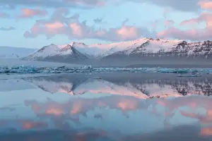 Panoramic view across the calm water of Jokulsarlon glacial lagoon towards snow-capped mountains and icebergs bathed in the last light of a winters afternoon, at the head of the Breidamerkurjokull Glacier on the edge of the Vatnajokull National Park, South Iceland, Iceland, Polar Regions