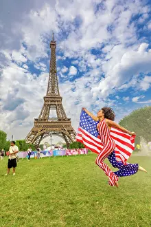 Patriotic American Woman jumping and cheering for Team USA and the Paris 2024 Olympics in front of the Eiffel Tower beach volleyball stadium, Paris, France, Europe