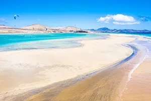 People kiteboarding on waves crashing on white sand of Sotavento beach, Fuerteventura