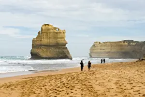People walk along a beach with one of the Twelve Apostles geological formation in the background
