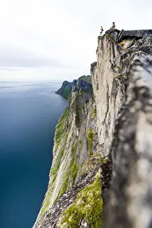 Adults Prints: Two people watching the blue water of the fjord standing on rocky peak of Segla mountain