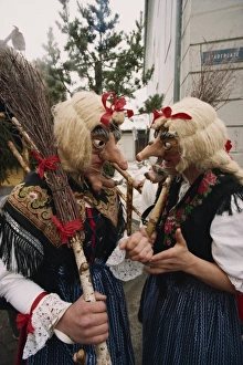 Masked Prints: Two people wearing masks and traditional dress, one carrying a broomstick