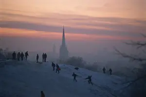 Norwich Prints: People in a winter landscape with snow on the ground and Norwich Cathedral in the background