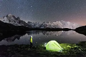 Mid Adults Prints: Person admiring the starry sky outside tent pitched on the shore of Cheserys lake surrounded by alpine landscape of
