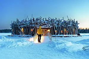 55 59 Prints: Person stands on the bridge connecting the main building of the illuminated Arctic Bath hotel made of logs