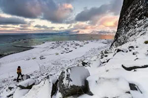 Photographer Prints: Photographer on the snow admires the fishing village under a colorful sky Eggum, Vestvagoy