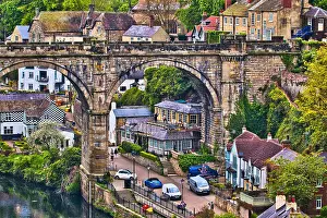 A picturesque view of a quaint village with an old stone bridge arching over a river, surrounded by lush greenery and traditional houses