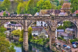 A picturesque view of a stone bridge arching over a river in a quaint village, surrounded by lush greenery and historic buildings