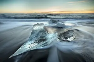 Pieces of glacier ice washed up on black volcanic sand beach at sunrise, near Jokulsarlon