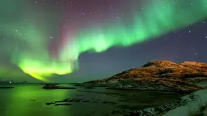 Pink and green aurora borealis (Northern Lights) photographed reflected in the sea near Tromso, Norway, Scandinavia, Europe