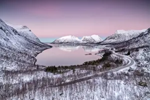 Pink sky at sunrise lights up the snowy peaks reflected in the cold sea, Bergsbotn