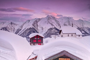 Pink sky at sunset frames the snowy mountain huts and church, Bettmeralp, district of Raron