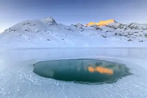 Lago Bianco Prints: The Piz Cambrena illuminated by the sun reflecting in a pool surrounded by ice at the Bernina