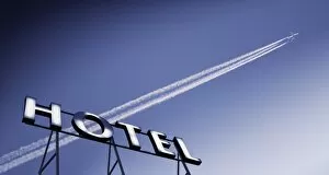 Plane in blue sky with vapour trail and hotel sign