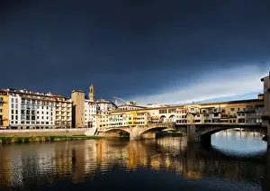 Ponte Vecchio reflecting in the Arno rRver against a dark blue stormy sky, Florence
