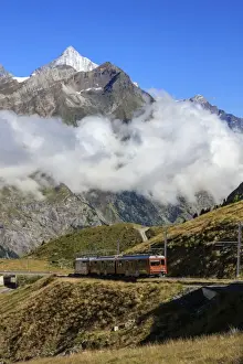 On The Move Prints: The red Bahn train proceeds with the peak of Dent Herens in the background, Gornergrat
