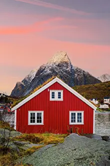 Cabin Prints: Red cabin with grass roof stands at sunset near mountains in Norway's Lofoten Islands