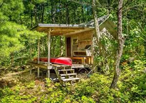 Retreat Prints: Red canoe resting in a cottage outbuilding surrounded by trees in Ontario