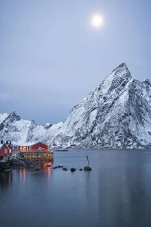 Nordland County Gallery: Red Rorbu cabins and majestic Olstind peak lit by moon during winter dusk, Hamnoy, Nordland county