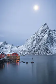 Light Beam Prints: Red Rorbu cabins and majestic Olstind peak lit by moon during winter dusk