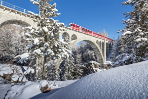 The red train on viaduct surrounded by snowy woods, Cinuos-Chel, Canton of Graubunden