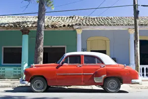 Parked Prints: Red vintage American car parked on street next to colourful buildings in Vinales