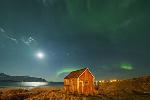 Nordland County Gallery: Red wood cabin on sand beach lit by moon during the Aurora Borealis (Northern Lights), Ramberg