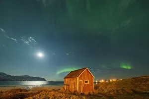 Nordland County Gallery: Red wood cabin on sand beach lit by moon during the Aurora Borealis (Northern Lights), Ramberg