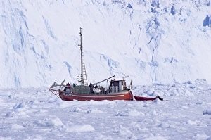 Red wooden boat crossing the ice in front of the Eqi Glacier