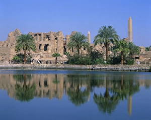 Reflections in the sacred lake of the temple, obelisks and palm trees at Karnak